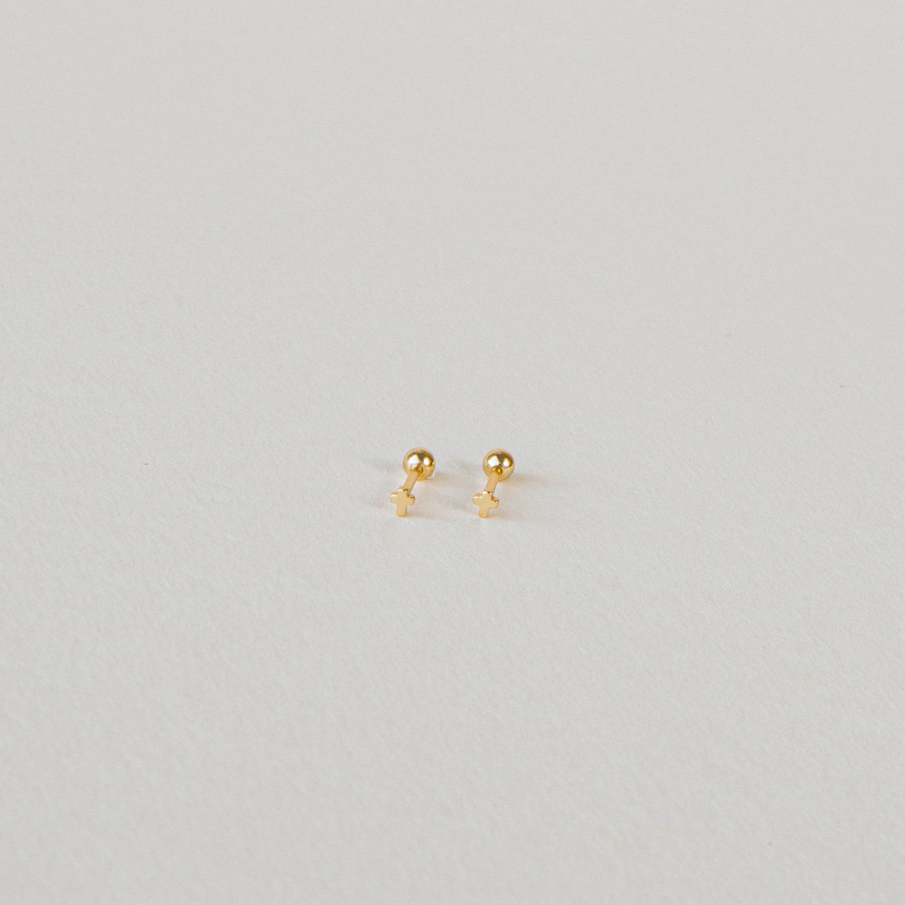 The Tiny Cross Studs are delicate stud earrings with small gold cross charms, shown against a plain white background.
