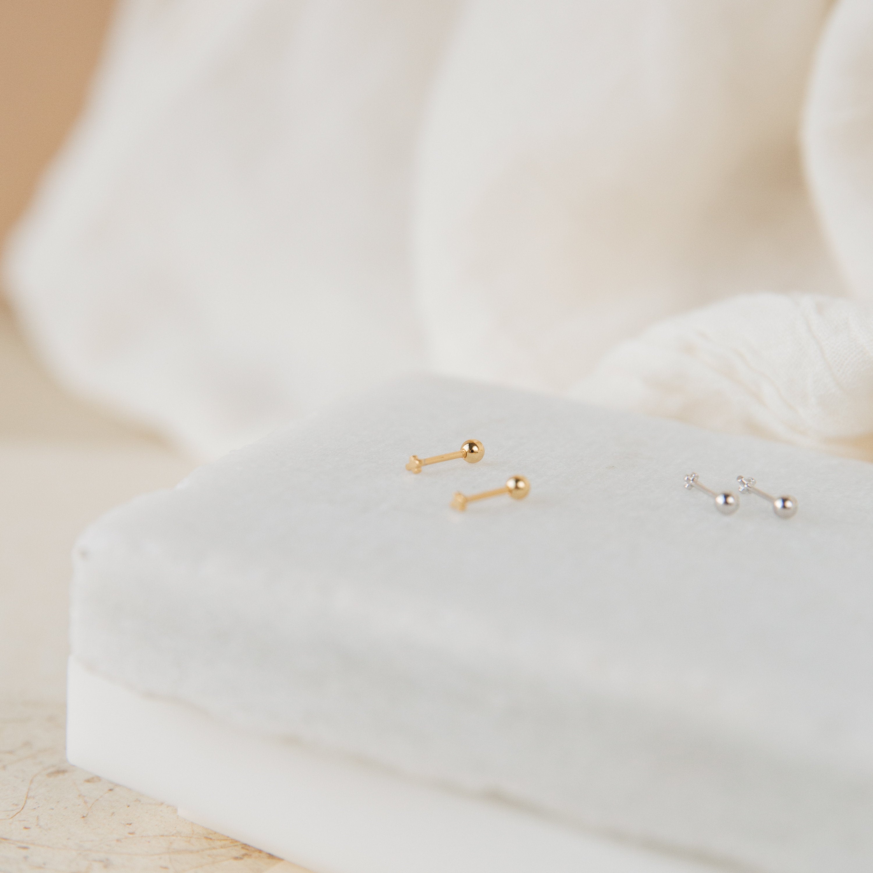 The Tiny Cross Studs in Sterling Silver are displayed on a white padded surface.