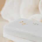 Tiny Cross Studs in gold and silver, displayed on a white, velvet-covered jewelry stand.