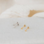 Two pairs of Tiny Heart Studs—one silver, one gold—are shown on a light textured surface. These earrings are perfect for everyday wear and make a thoughtful gift for someone special.
