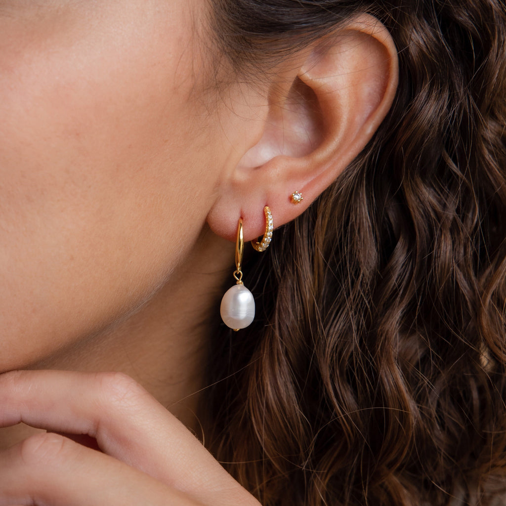 A gold Dangling Pearl Drop Earring styled in a multiple-piercing ear stack with pavé gold hoops and a diamond stud. 