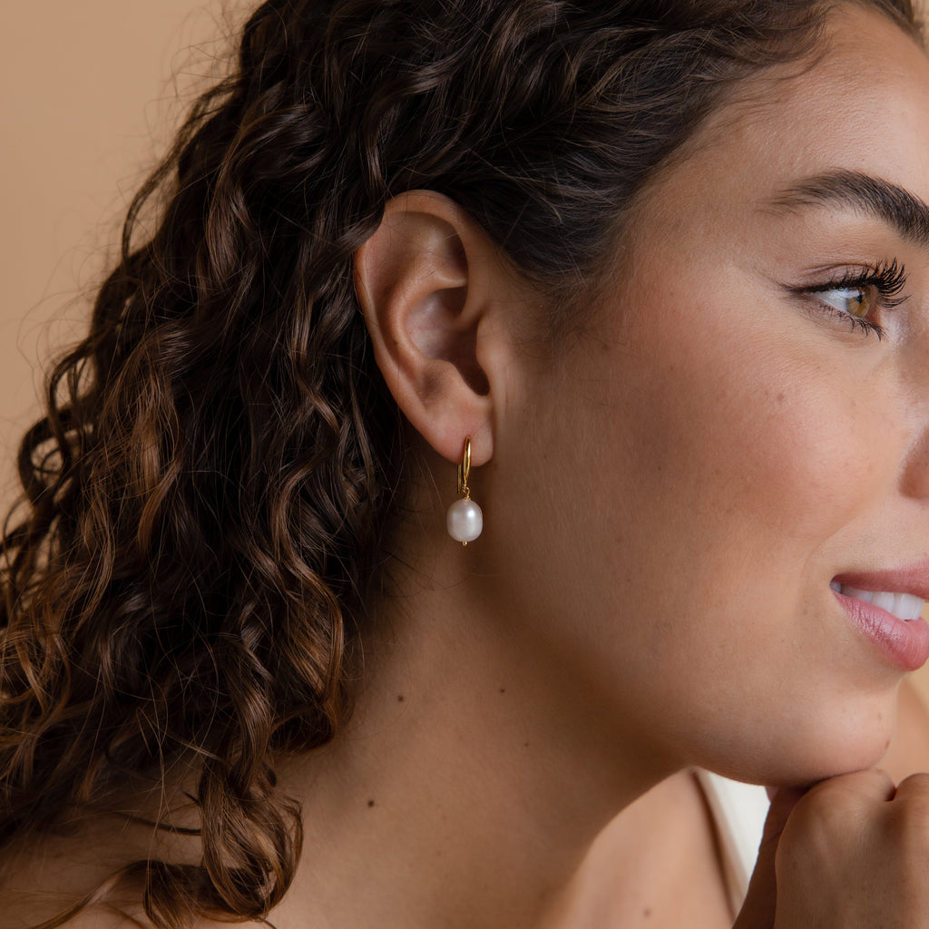 A smiling woman models one of the gold Dangling Pearl Drop Earrings