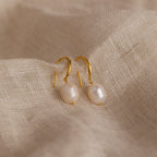 Gold Dangling Pearl Drop Earrings arranged neatly on a beige woven textile background.