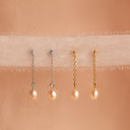 Two pairs of Isha Pink Pearl Earrings—one with silver dangling chains and one with gold—are displayed on soft fabric.