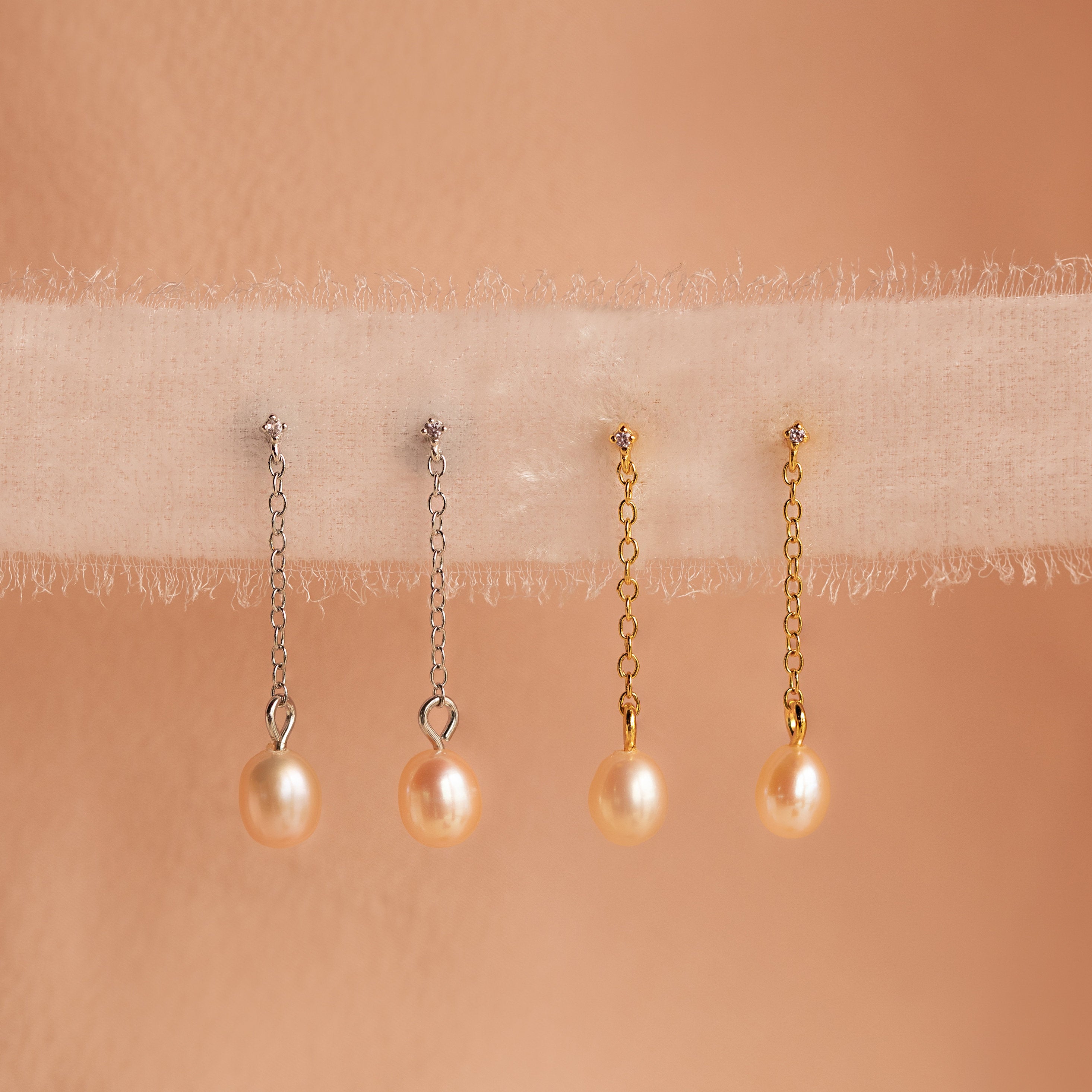 Two pairs of Isha Pink Pearl Earrings—one with silver dangling chains and one with gold—are displayed on soft fabric.