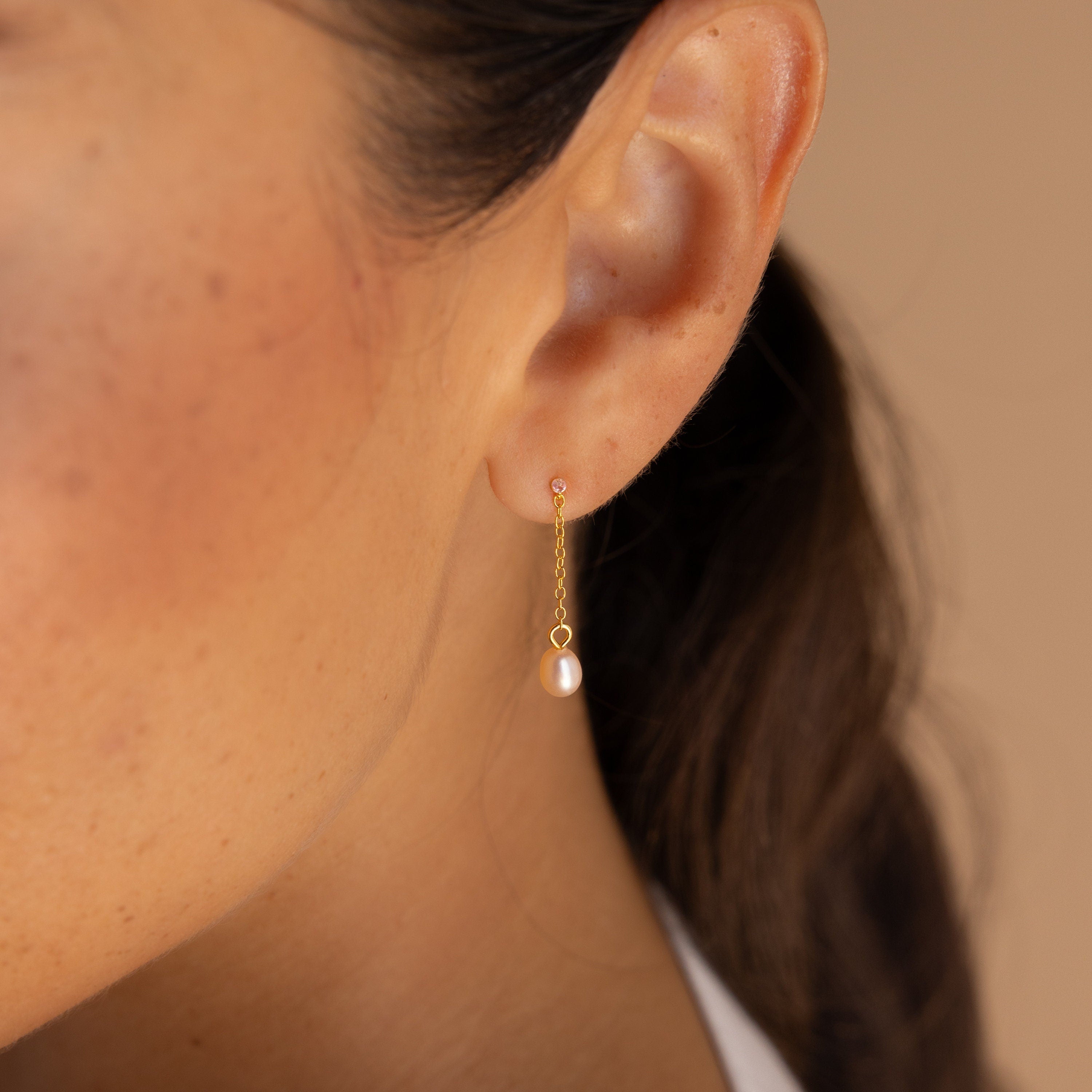 Close-up of a woman's ear wearing the Isha Pink Pearl Earrings, featuring dangling chains and a delicate pink pearl drop that highlights their elegant design.