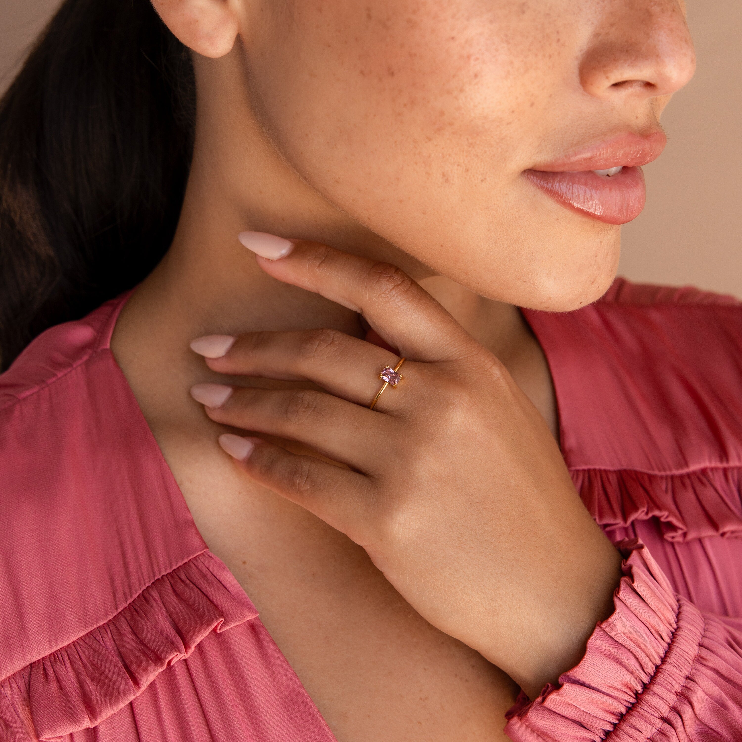 A woman in a pink top displays the Blush Pink Emerald Ring, showcasing its gold band and pink stone on her finger.