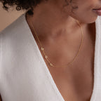 A woman wearing the Sideways Initial Necklace in gold with a white V-neck top.