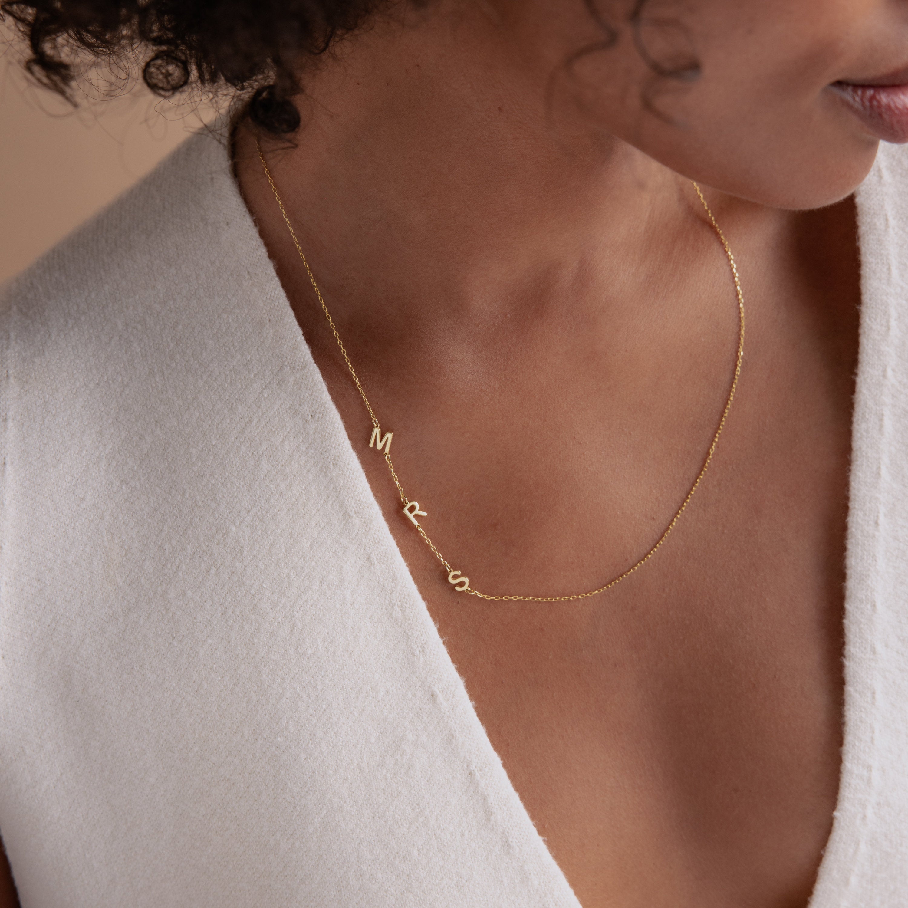 A woman wearing the Sideways Initial Necklace in gold with a white V-neck top.