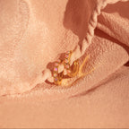 Pink Opal Huggies, elegant gold hoop earrings with pastel gemstones, are displayed on soft peach-colored fabric for a chic, feminine jewelry showcase.