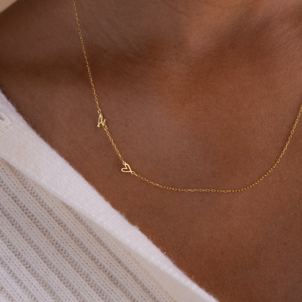 The Sideways Initial Heart Necklace features an "A" and heart pendant, stylishly layered over a white textured garment for a unique personalized accent.