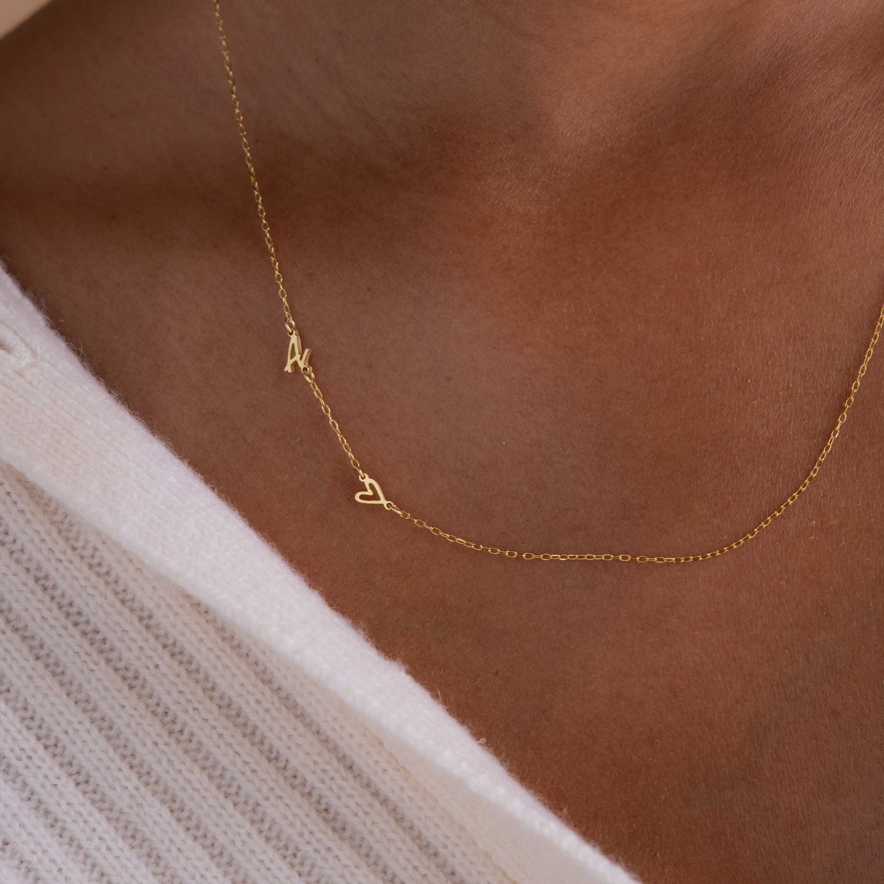 The Sideways Initial Heart Necklace features an "A" and heart pendant, stylishly layered over a white textured garment for a unique personalized accent.
