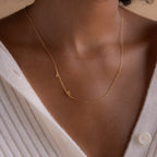 A person in a white ribbed button-up top wears the Sideways Initial Heart Necklace, featuring a gold A and heart pendant.