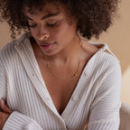 Woman with curly hair wearing a white ribbed sweater and the Duo Initial Necklace in Box Chain—a gold charm necklace featuring the letters S and R.