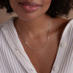 A woman wearing a white sweater and the Duo Initial Necklace in Box Chain with A and T letter charms.