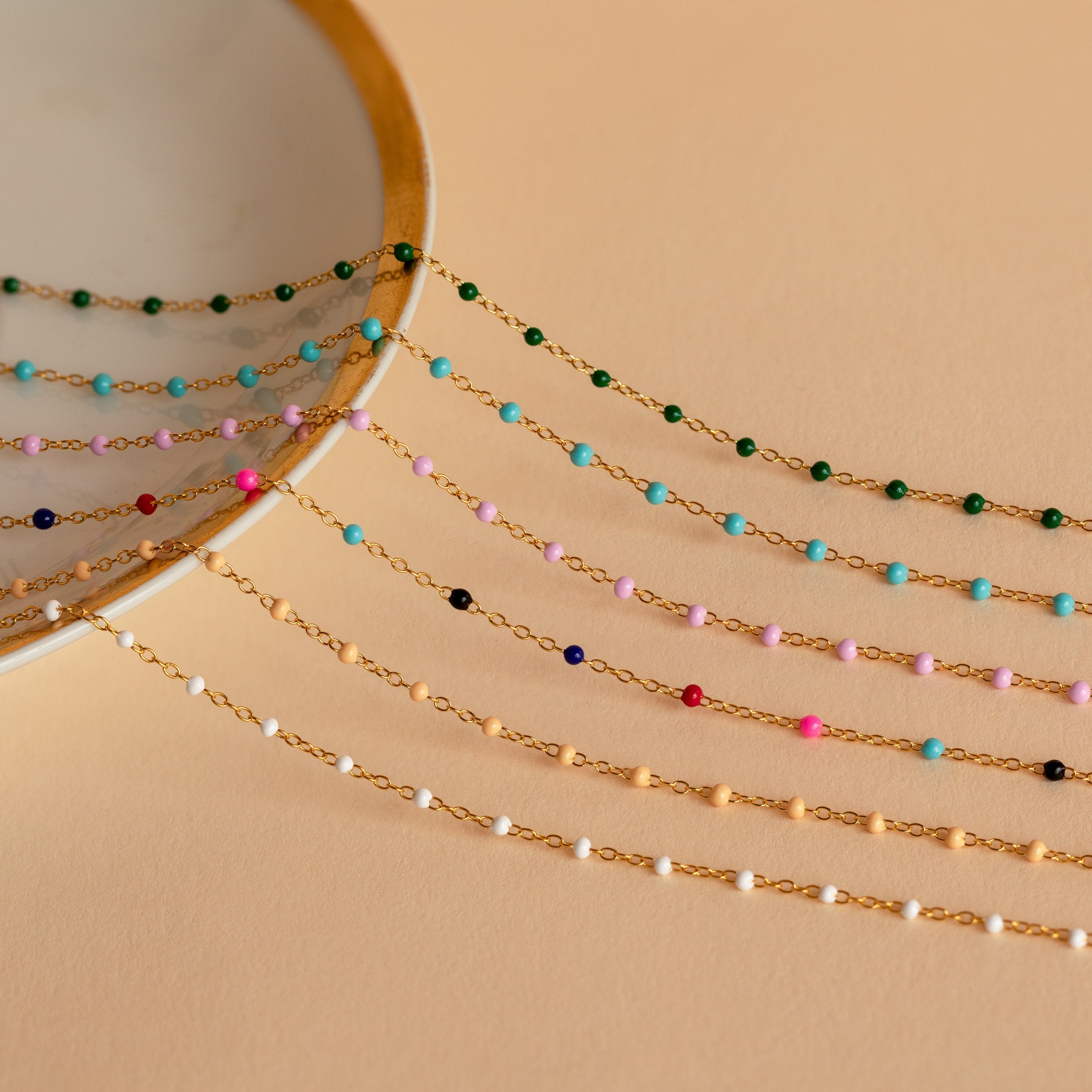 The Pink Station Necklace features colorful beads and dainty chains, elegantly draped over a round mirror on a beige background—perfect for necklace layering lovers.