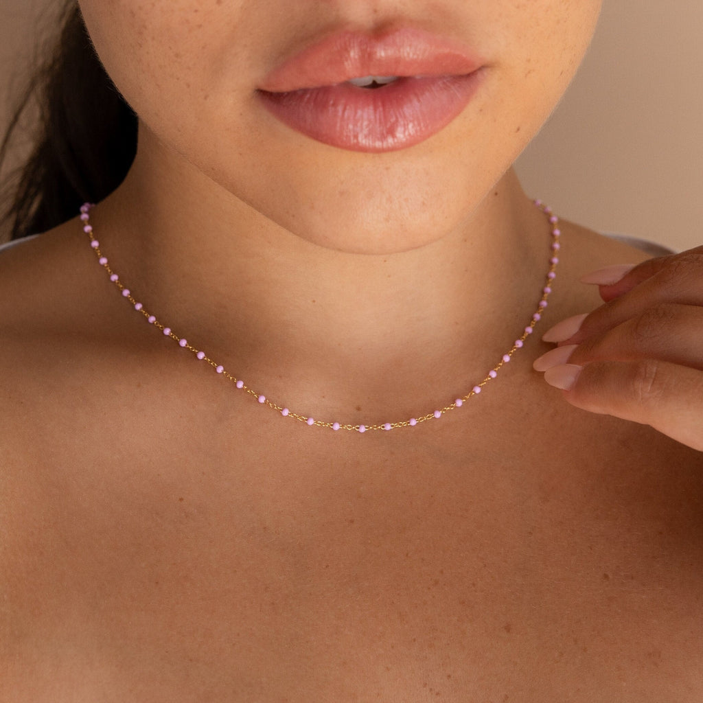 A woman touches her Pink Station Necklace with her hand, showing only her lips and neck.