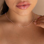A woman touches her Pink Station Necklace with her hand, showing only her lips and neck.