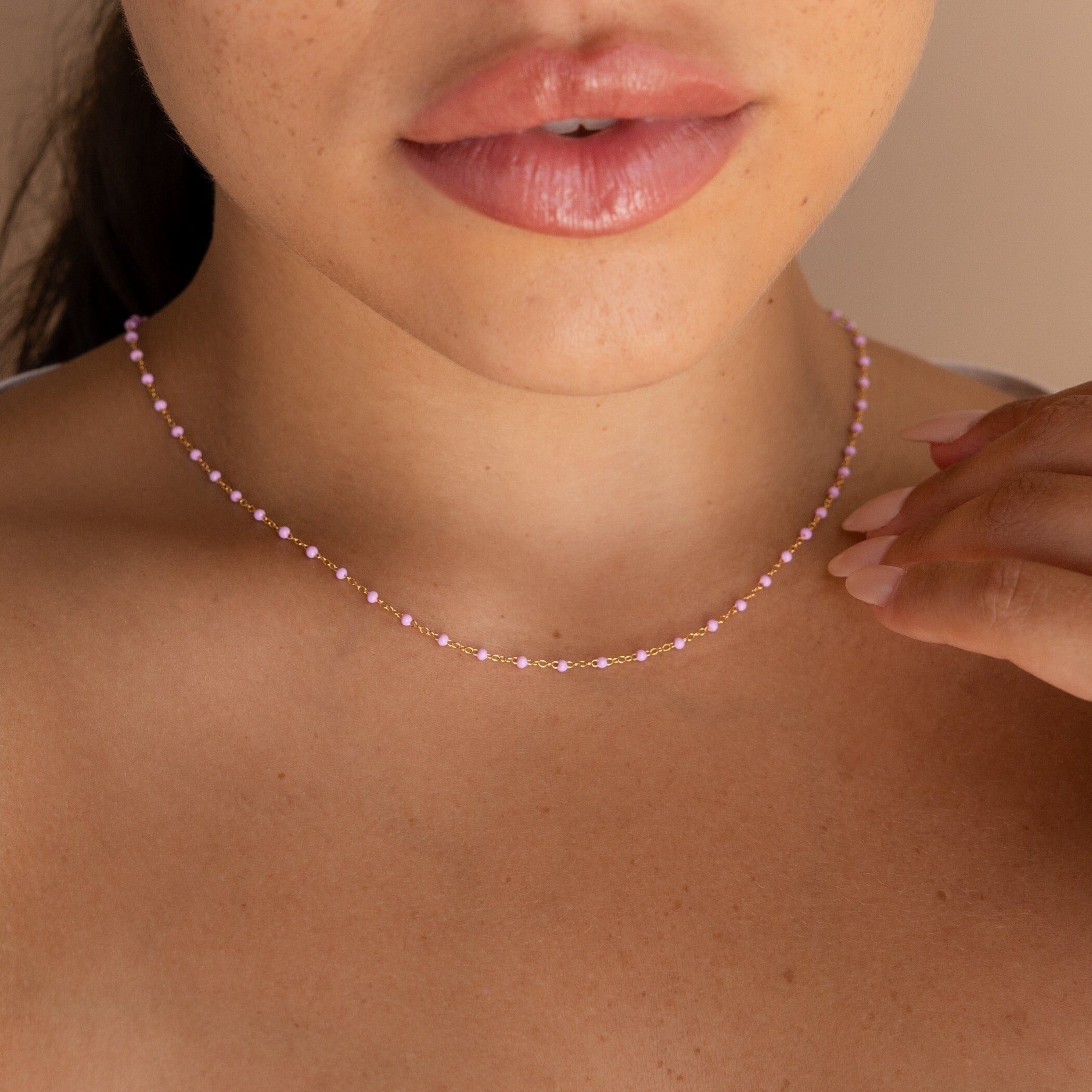 A woman touches her Pink Station Necklace with her hand, showing only her lips and neck.