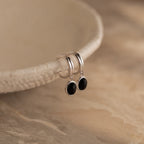 Black Gemstone Drop Hoops with dangling black oval stones rest on a textured beige dish—perfect as stylish everyday earrings or striking black gemstone accents for any occasion.