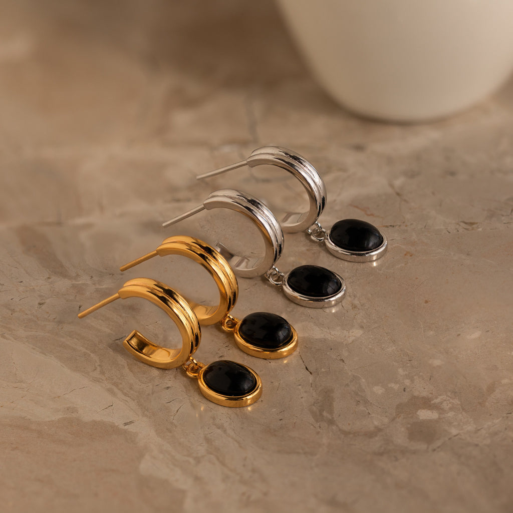 Two pairs of Black Gemstone Drop Hoops, one gold and one silver, each with a black gemstone pendant, on a marble surface. Ideal for adding everyday elegance to any look.