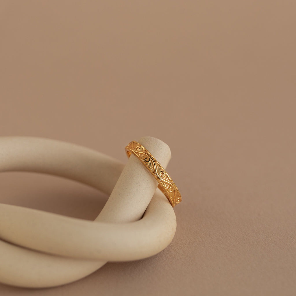 Gold filigree ring elegantly draped over a matte ceramic spiral, showcasing engraved pattern and polished finish.