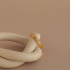 Gold filigree ring elegantly draped over a matte ceramic spiral, showcasing engraved pattern and polished finish.