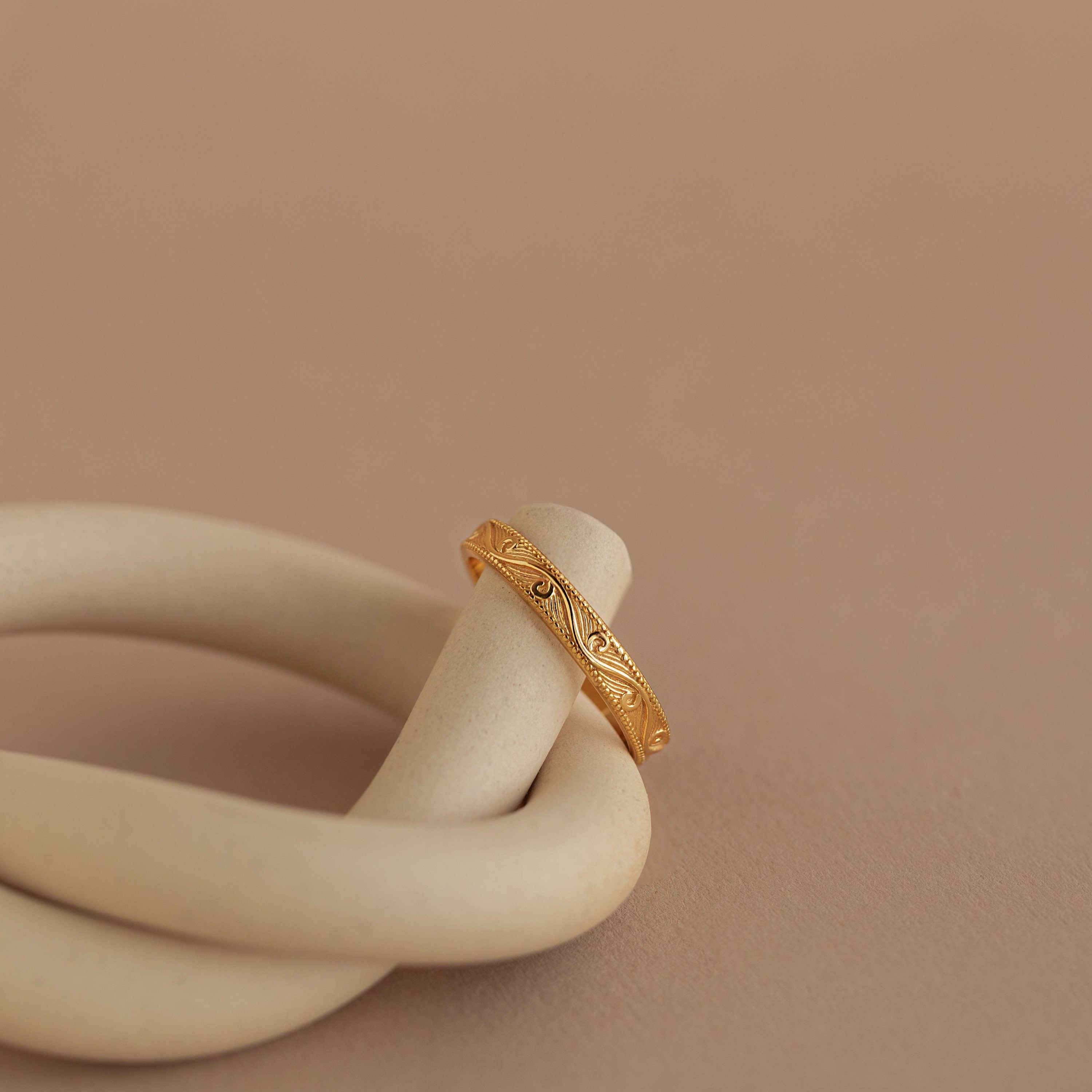 Gold filigree ring elegantly draped over a matte ceramic spiral, showcasing engraved pattern and polished finish.