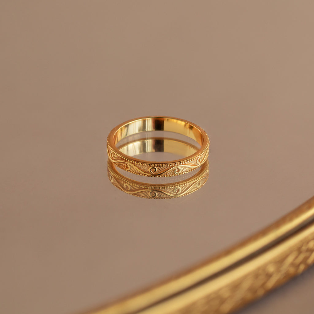 Gold filigree ring with intricate pattern, reflected on a polished mirror surface.