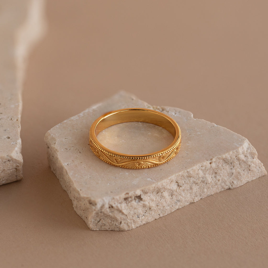 Detailed gold filigree ring displayed on a textured stone slab.