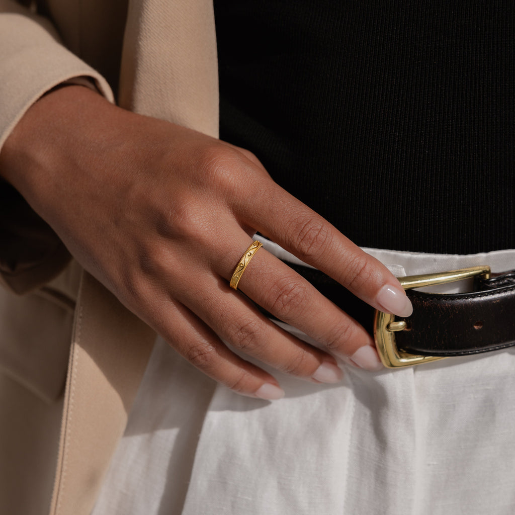 Gold engraved filigree ring shown on model’s hand styled with high-waisted trousers and a tailored beige blazer.