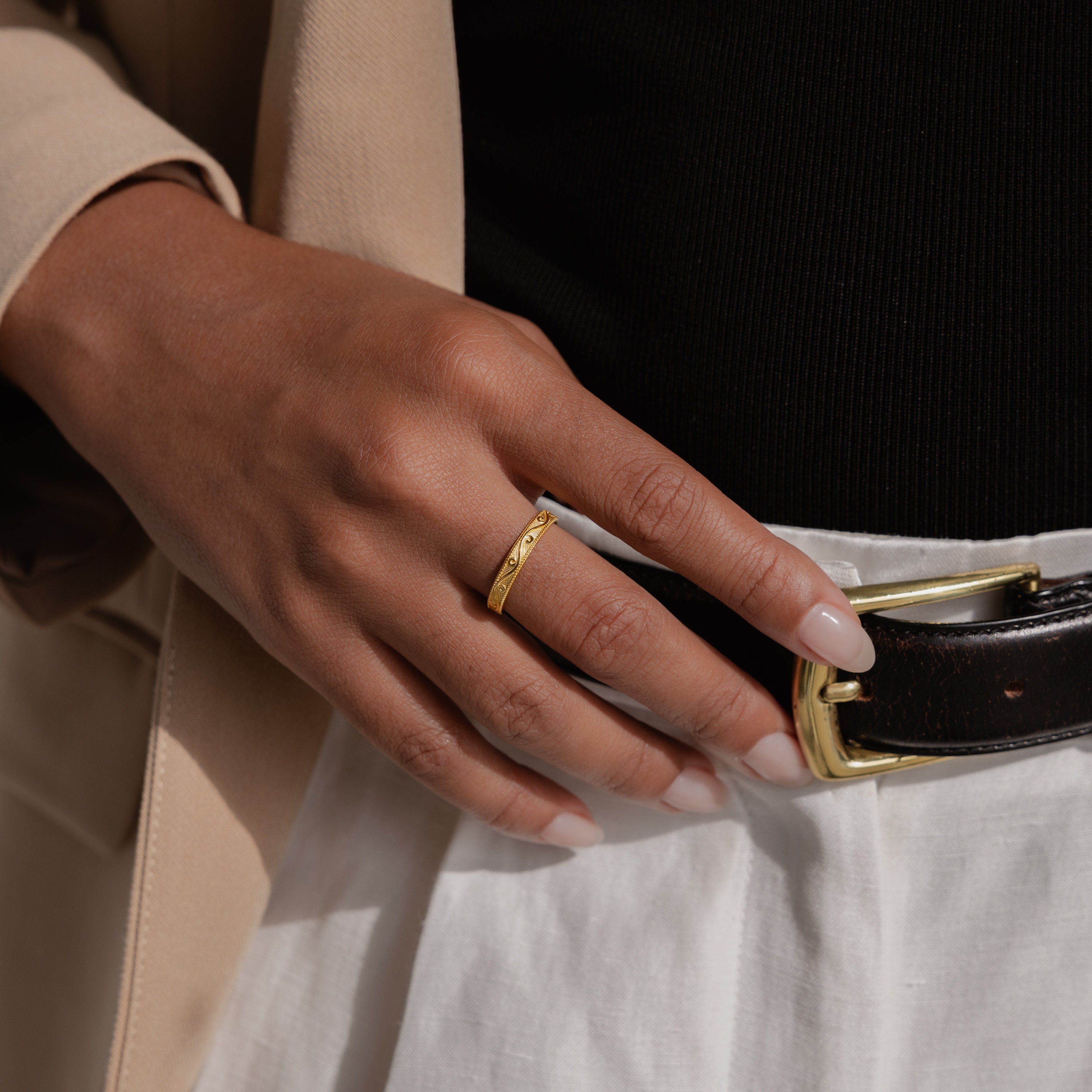 Gold engraved filigree ring shown on model’s hand styled with high-waisted trousers and a tailored beige blazer.