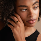 A woman with curly hair touches her face, highlighting the Black Curve Ring Set with dark stones, complemented by a sleeveless black top.