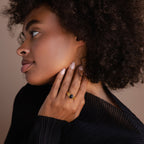 A woman with curly hair in a black top shows off a Celestial Black Signet Ring on her finger—an elegant statement piece—as she gazes thoughtfully to the side.