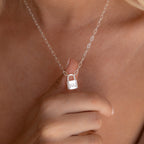 A person holds an Initial Padlock Paperclip Necklace, a silver chain with a small padlock pendant engraved with SVJ—an elegant personalized necklace ideal for couples.
