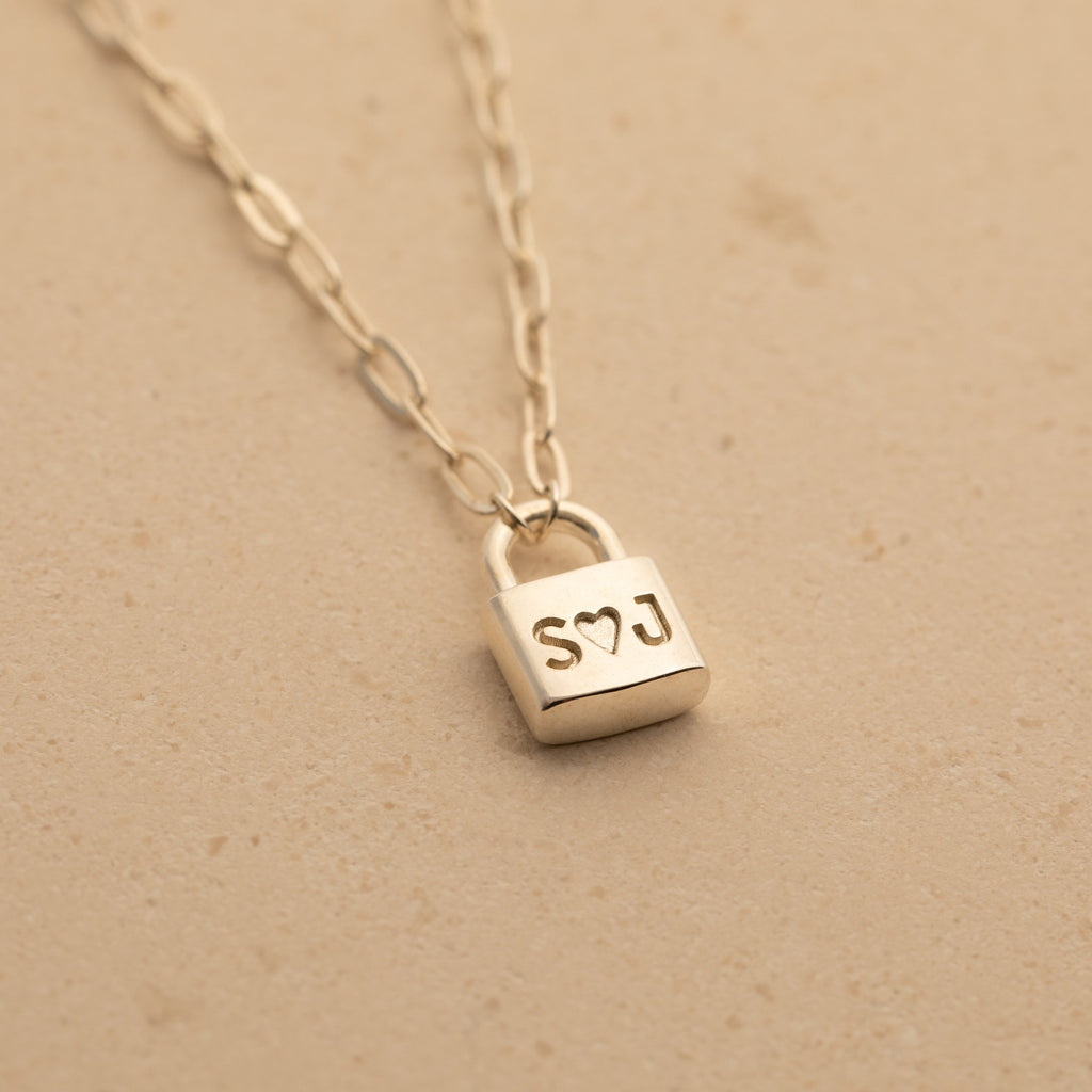 Initial Padlock Paperclip Necklace featuring a personalized padlock pendant engraved with S♡J, perfect for couples and beautifully displayed on a beige surface.