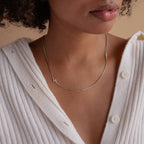 A woman wears a white sweater and the Sideways Initial Necklace In Box Chain, featuring a silver H pendant.