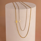 Two gold Sideways Initial Necklaces in box chain and one silver with letter pendants B and H, displayed on a cylinder—perfect for adding an initial touch to any style.