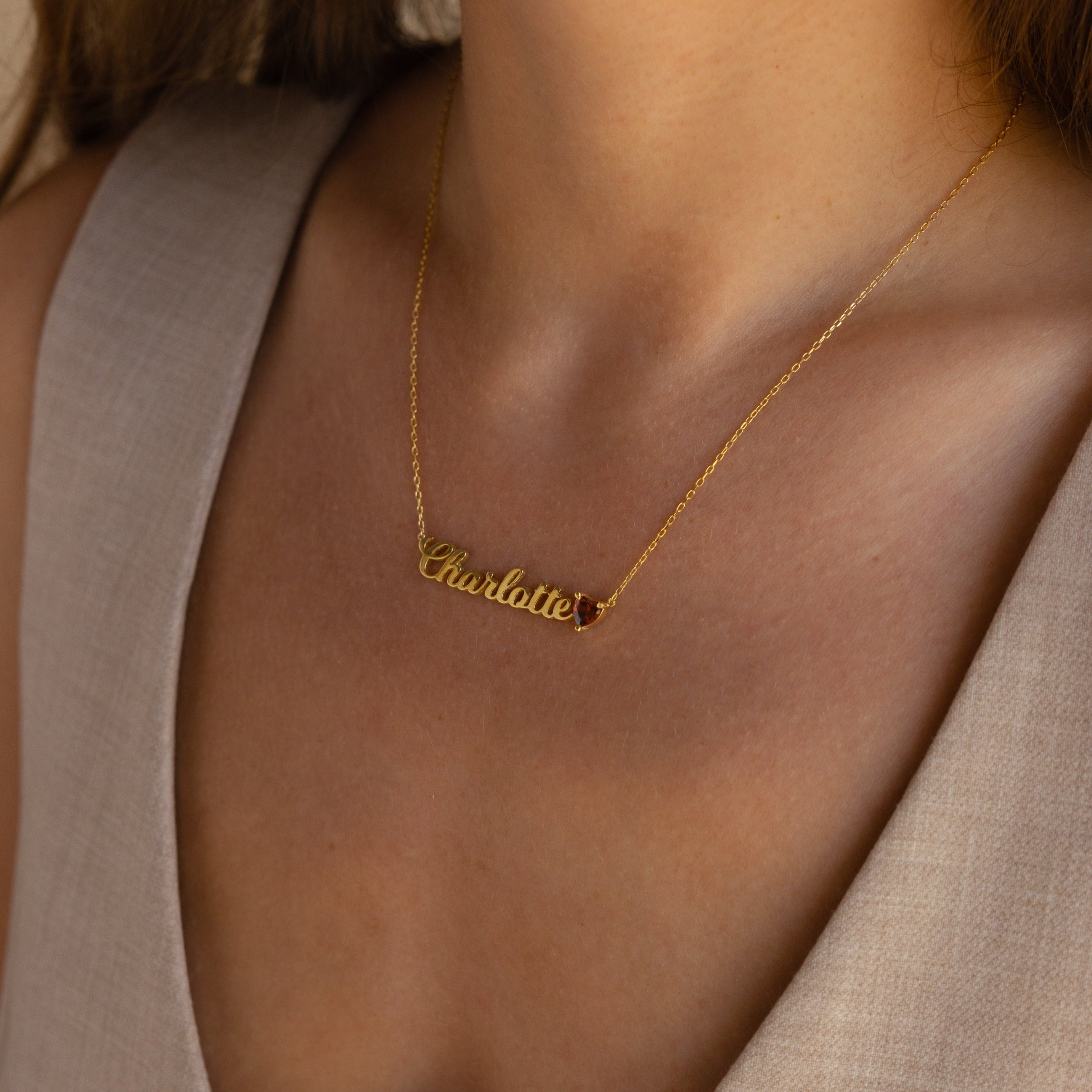 The Mellow Name Heart Birthstone Necklace featuring "Charlotte" sits elegantly on a woman's neck, beautifully complementing her beige v-neck top—a perfect choice for Minimalist Jewelry enthusiasts.