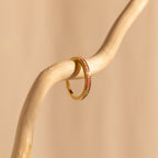 The Pink Opal Inlay Band, featuring a green inlay, is displayed on a curved light wooden branch set against a beige background.