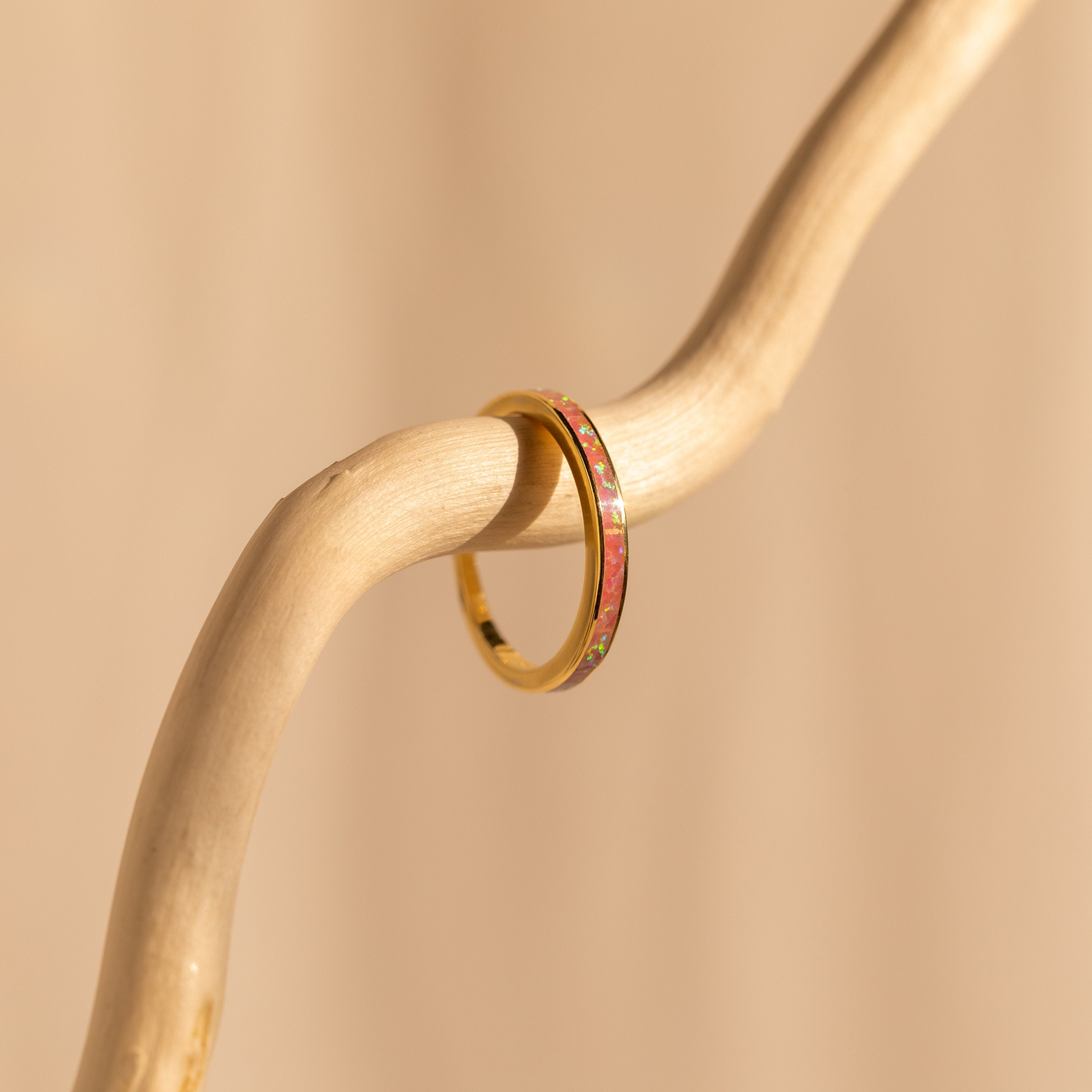 The Pink Opal Inlay Band, featuring a green inlay, is displayed on a curved light wooden branch set against a beige background.