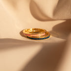 The Pink Opal Inlay Band features a delicate gemstone set in a dainty ring, shown glowing warmly as it rests on soft beige fabric in the sunlight.