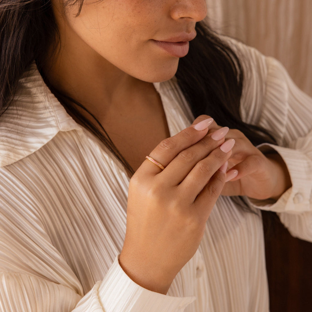 Woman in a cream pleated blouse displays the Pink Opal Inlay Band on her finger, hands near her chest.