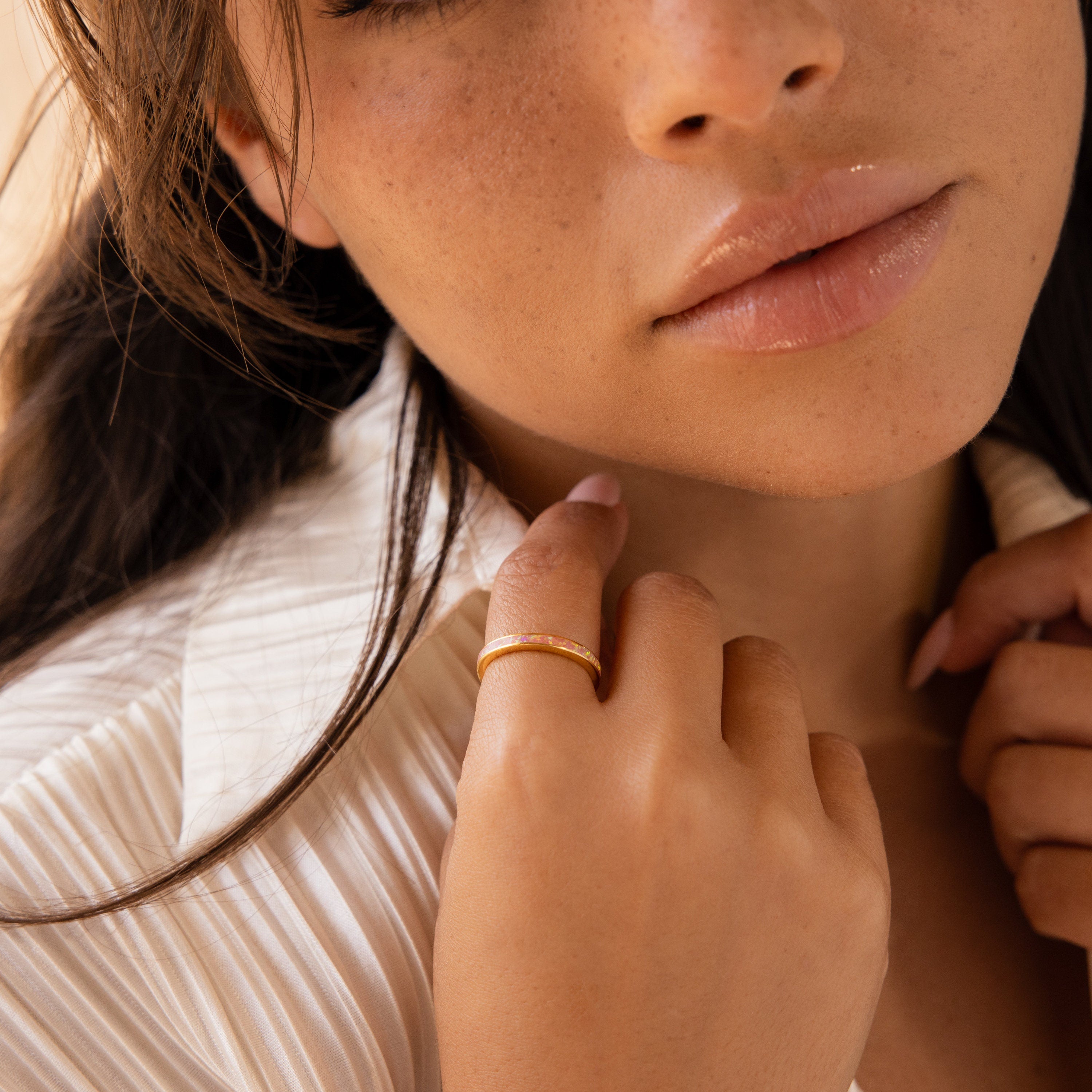 A woman in a white shirt gently touches her collar, showcasing the Pink Opal Inlay Band on her finger, with natural makeup and soft lighting.