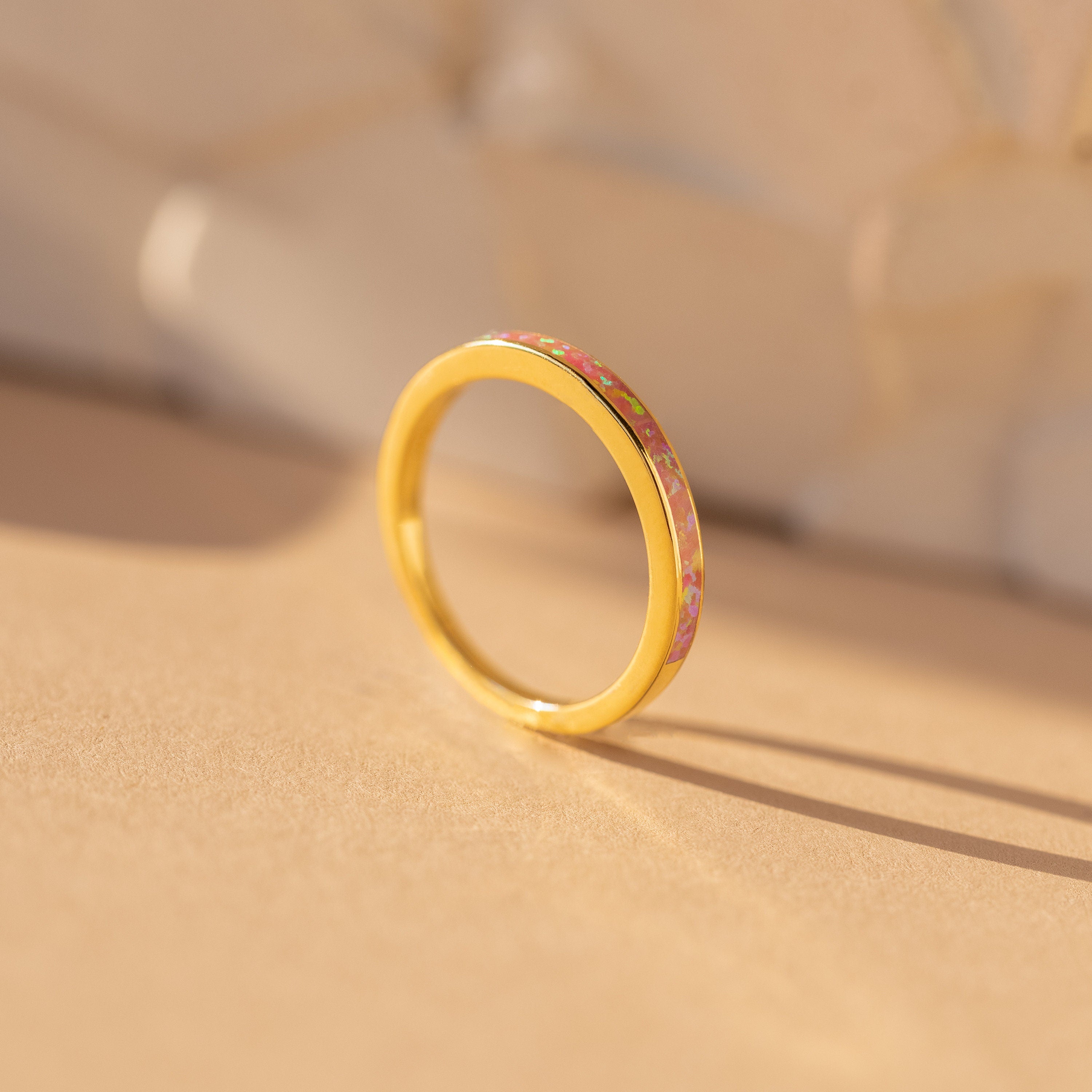 The Pink Opal Inlay Band features a pink and yellow floral inlay, displayed upright on a beige surface with a soft shadow, adding an elegant and feminine touch.