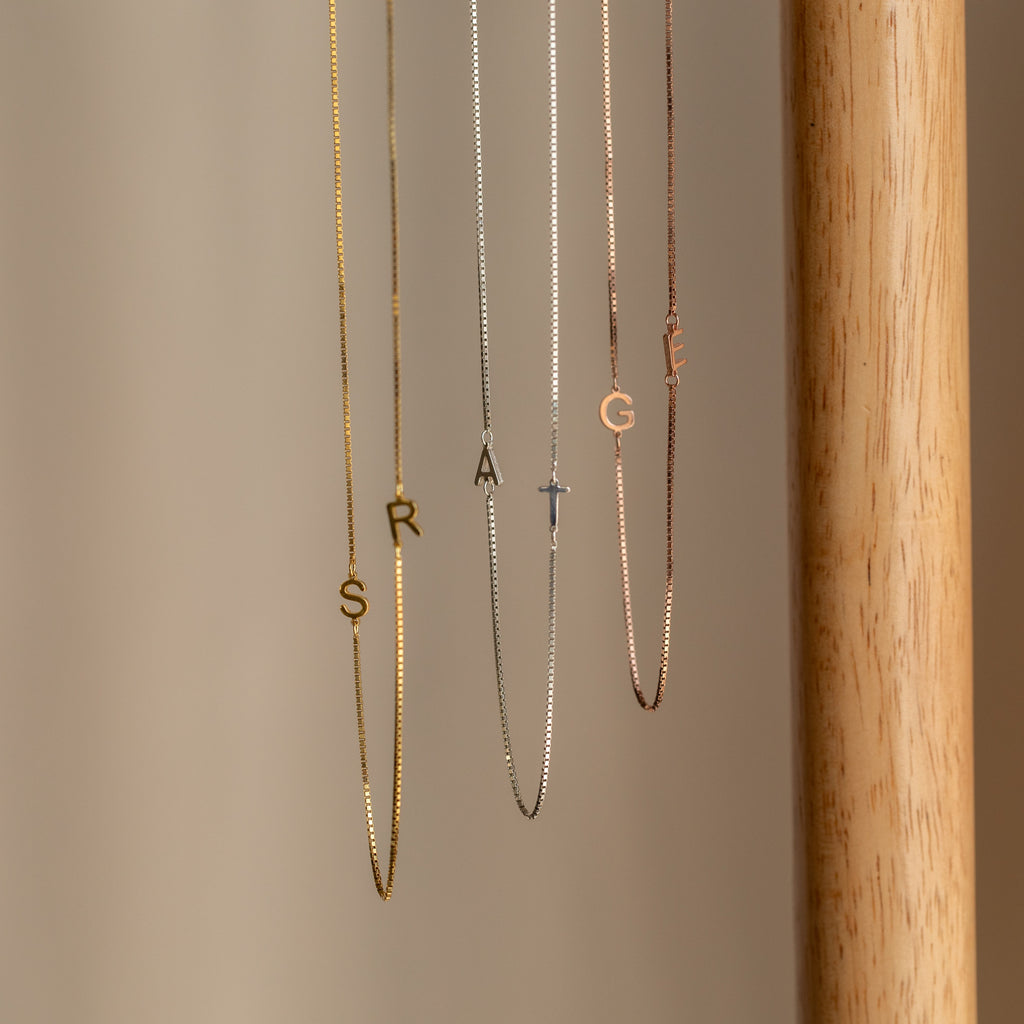 Two Duo Initial Necklaces in Box Chain display personalized letter charms spelling STRANGE, set against a neutral background.