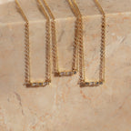 Three Initial Morse Code Necklaces, featuring rectangular gemstone pendants for personalized jewelry, are elegantly displayed on a marble surface.
