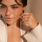 Woman with freckles wears a beige sweater and the Custom Pave Hexagon Ring, gazing slightly to the side in soft light.