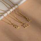 Three Gothic Pave Initial Necklaces with jeweled r, m, and e pendants rest on a beige surface—showcasing personalized jewelry in striking Gothic style.