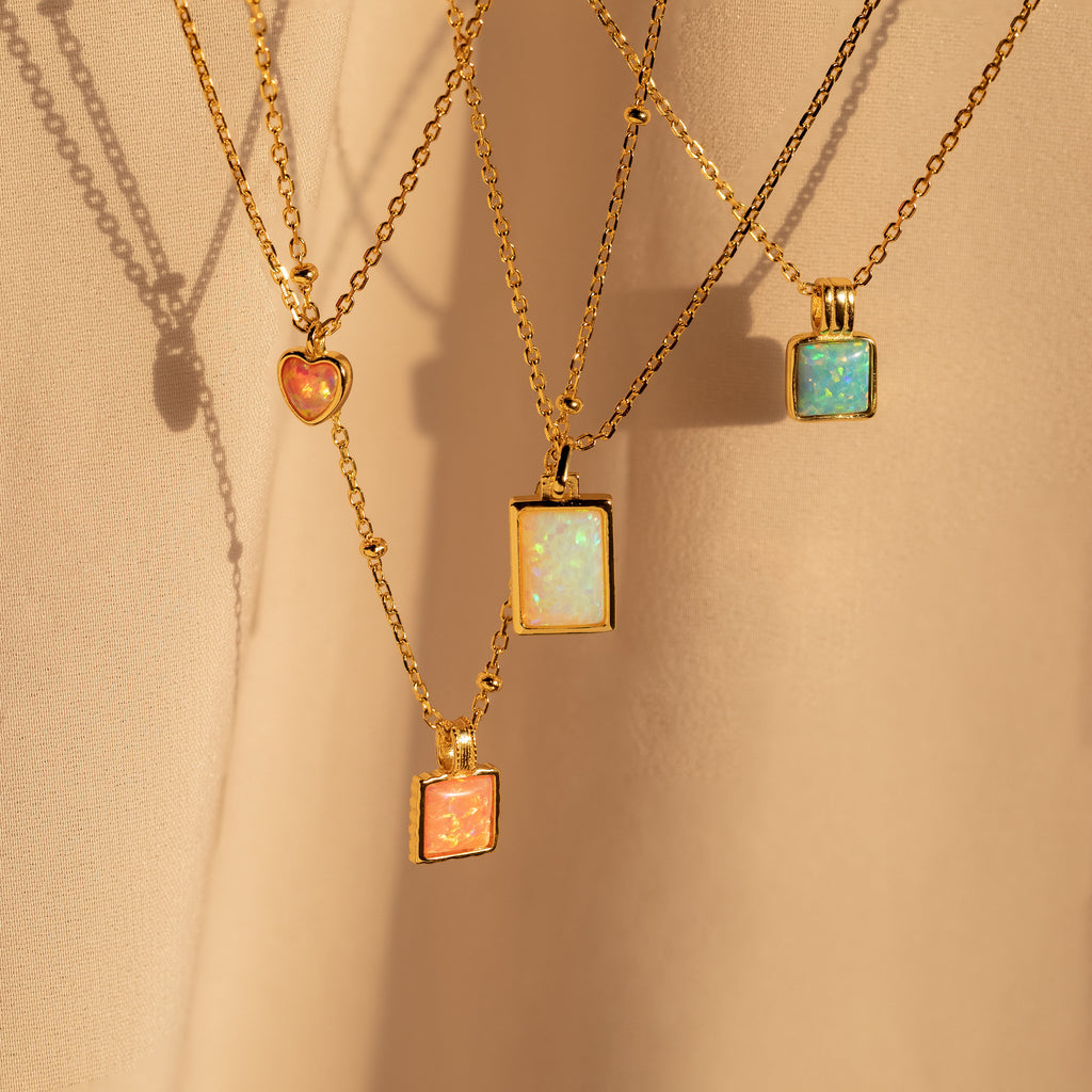 Four gold chain necklaces, including the Pink Opal Pendant Necklace, are displayed on a soft beige fabric background.
